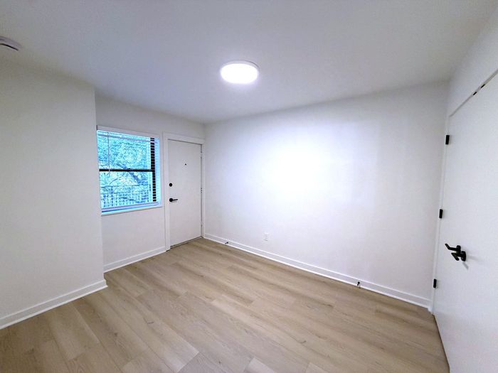 Bright and inviting room with modern light wood flooring, showcasing a window with leafy views and sleek white walls.