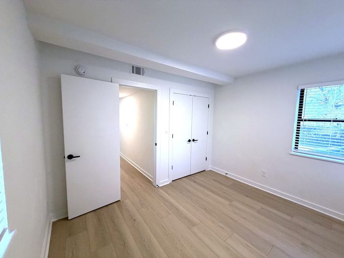Bright and airy room featuring sleek wooden floors, modern door, and large window with blinds.