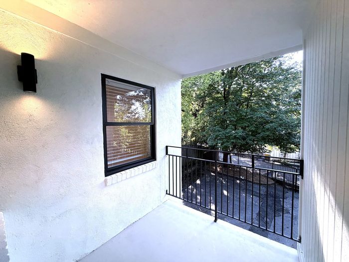 Charming apartment balcony with elegant black railing, offering a serene view of lush green trees and a cozy outdoor atmosphere.