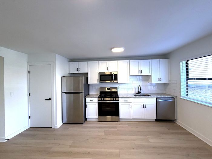 Modern kitchen with stainless steel appliances, sleek white cabinets, and elegant countertops, complemented by light wood flooring and natural light from a large window.