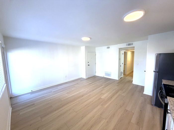 Bright, open living area with elegant wooden flooring, modern lighting, and a sleek stainless steel refrigerator.