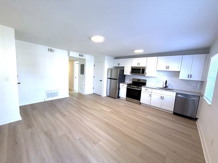 Modern apartment interior with an open-concept kitchen featuring sleek white cabinetry, stainless steel appliances, and light wood flooring.