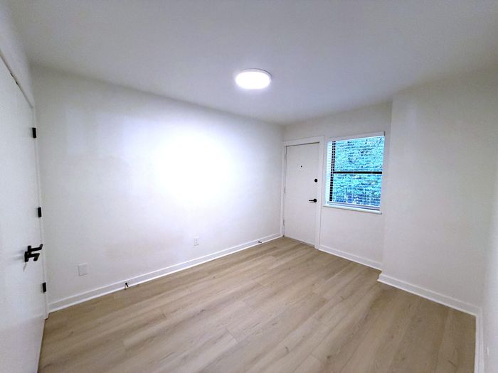Bright and modern bedroom featuring sleek hardwood flooring and a large window, perfect for natural light.