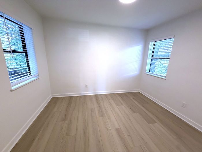 Bright and airy empty room with two large windows, elegant wood flooring, and freshly painted white walls.