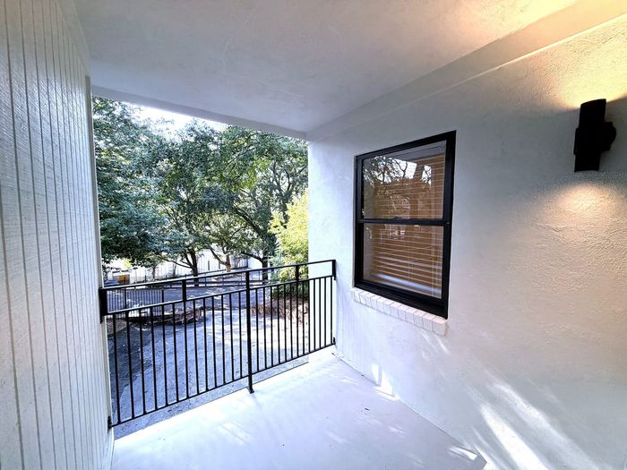 Inviting apartment balcony with sleek railing, offering serene views of lush greenery and natural light.