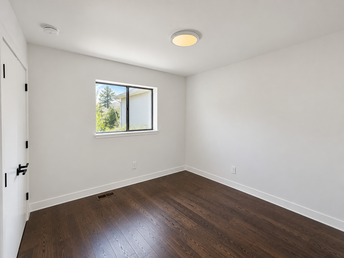 Bright and inviting room featuring elegant hardwood flooring, a large window allowing natural light, and minimalist white walls.