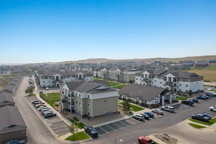 Scenic aerial view of a modern apartment complex with lush green courtyards, ample parking, and picturesque surroundings.
