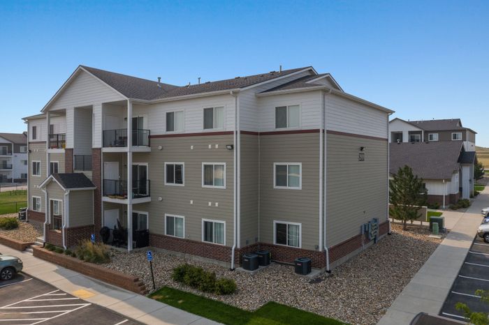 Modern multi-story apartment building with stylish balconies, surrounded by well-maintained landscaping and ample parking space. Ideal for contemporary living.