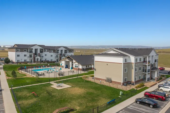 Modern apartment complex with spacious units, swimming pool, and landscaped outdoor area on a sunny day.
