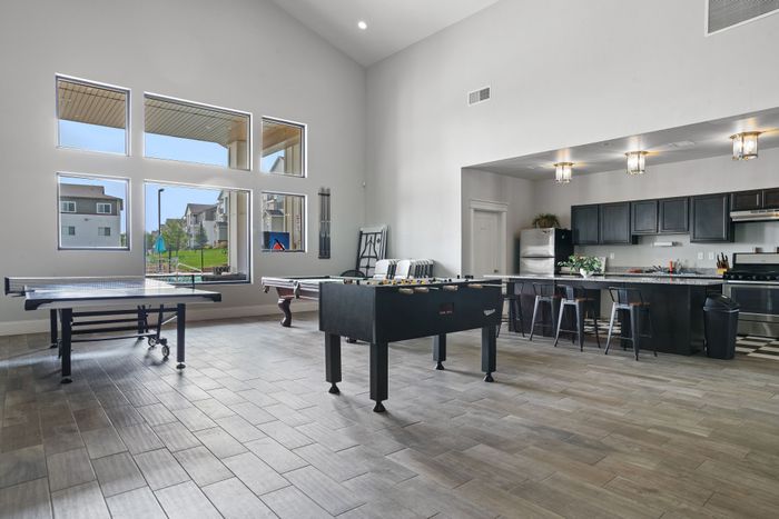 Modern recreational area featuring a foosball, ping-pong, and pool table with a stylish open kitchen and bar seating, perfect for entertaining.