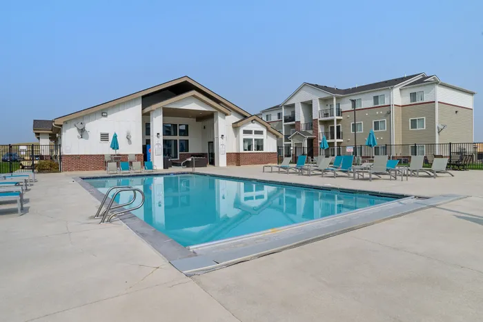 Modern apartment complex featuring a luxurious outdoor pool with stylish loungers and a contemporary clubhouse.