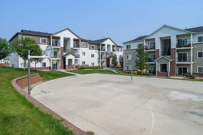 Charming apartment complex with modern architecture, featuring spacious balconies and a community basketball court surrounded by lush greenery.