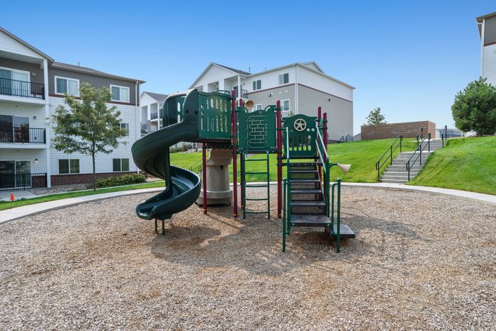 Inviting community playground with a fun spiral slide, nestled among charming apartment buildings and lush green scenery.