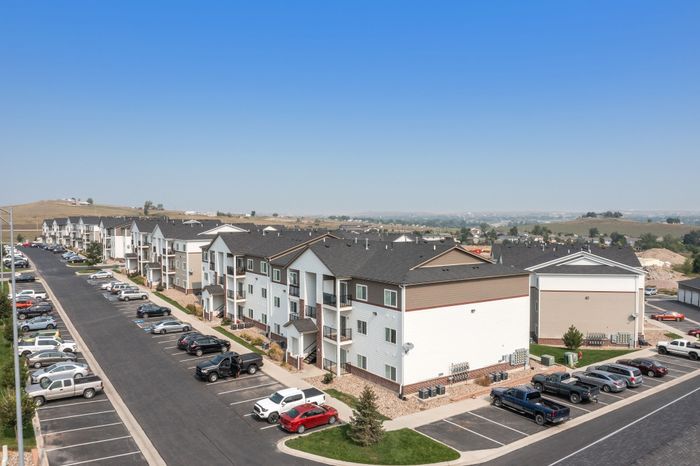 Charming apartment complex with modern architecture and ample parking, surrounded by scenic views and clear blue skies.