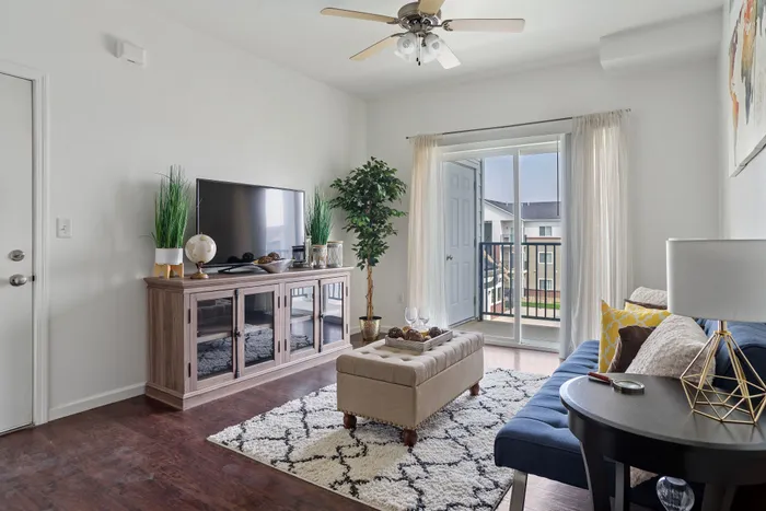 Bright and inviting apartment living room with modern decor, hardwood floors, and a cozy seating area. Large sliding doors open to a balcony, flooding the space with natural light.