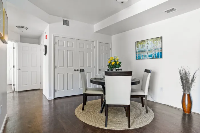 Modern dining area with elegant round table, stylish chairs, and vibrant floral centerpiece, set against a bright and airy interior with pristine white walls and dark hardwood flooring.