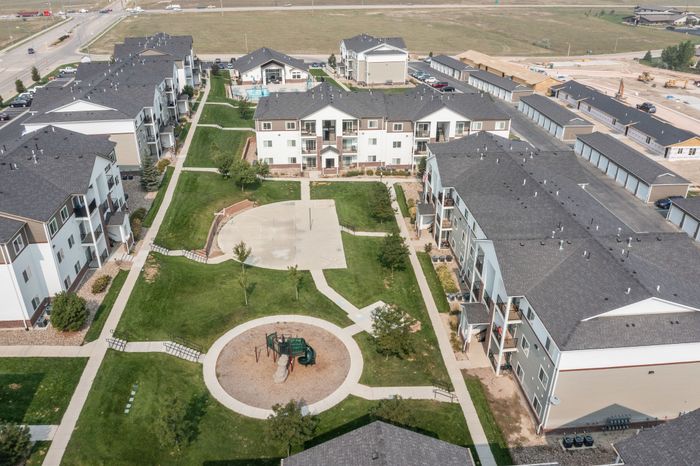 Bird's-eye view of a modern apartment complex featuring beautifully landscaped grounds, a playground, and ample parking.