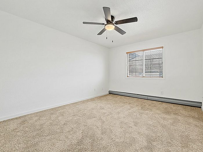 Bright and spacious bedroom with plush carpeting, modern ceiling fan, and ample natural light from large window.