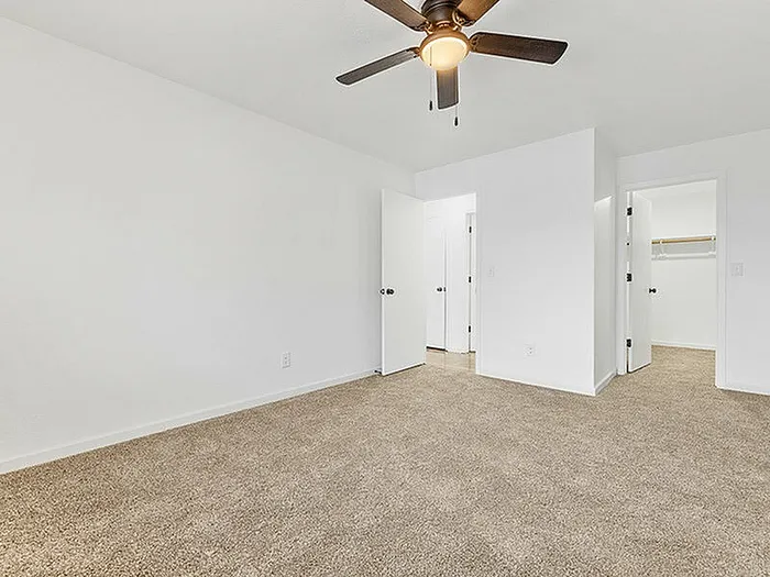 Spacious bedroom with plush carpet, stylish ceiling fan, and adjoining walk-in closet in a modern apartment.
