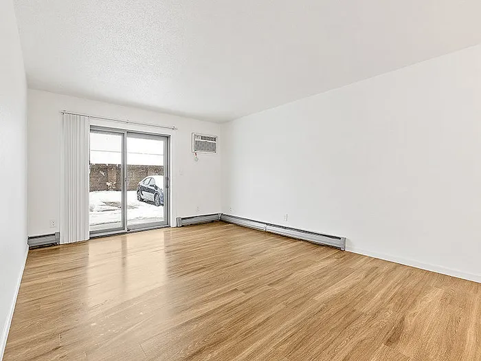 Bright living room with elegant hardwood floors, large window, and sliding glass door leading to a snowy outdoor view.