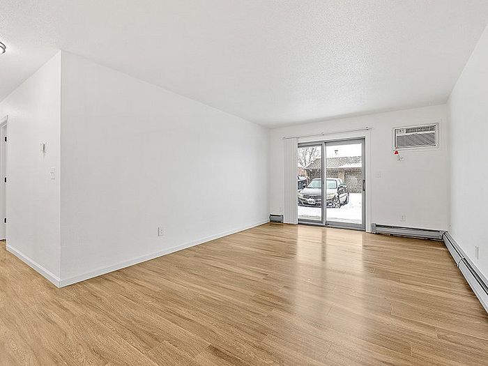 Bright and spacious living room featuring sleek hardwood floors, modern white walls, and large sliding glass doors leading to a scenic view.