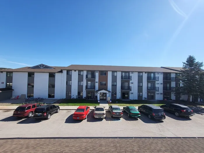 Charming three-story apartment building with ample parking and modern exterior, set against a clear blue sky.