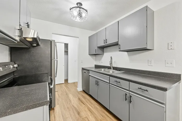 Modern kitchen with sleek gray cabinetry, stainless steel appliances, and elegant lighting, enhancing the warmth of the wood-style flooring.