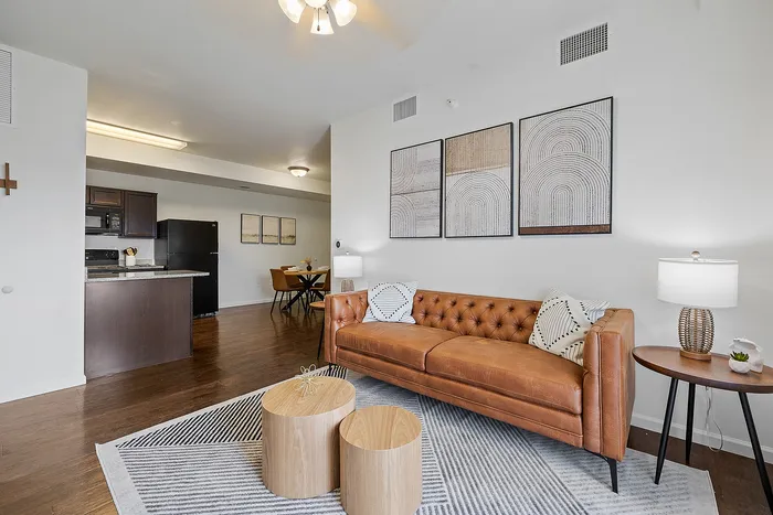 Modern apartment living space with elegant leather sofa, chic decor, and open-concept kitchen and dining area.