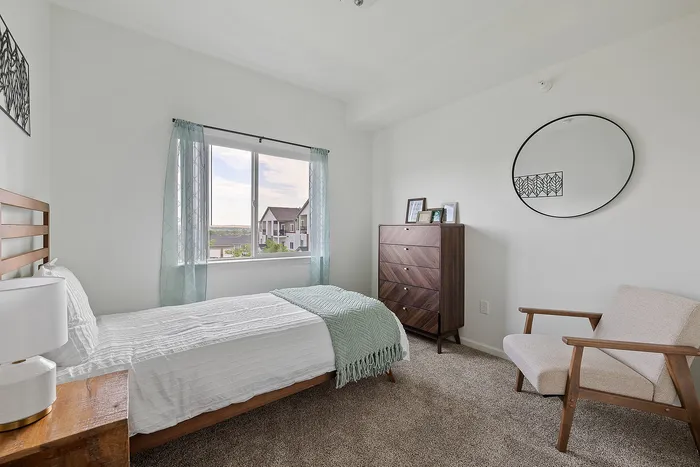 Bright and cozy bedroom with stylish decor, featuring a single bed, elegant dresser, and large window with scenic views.