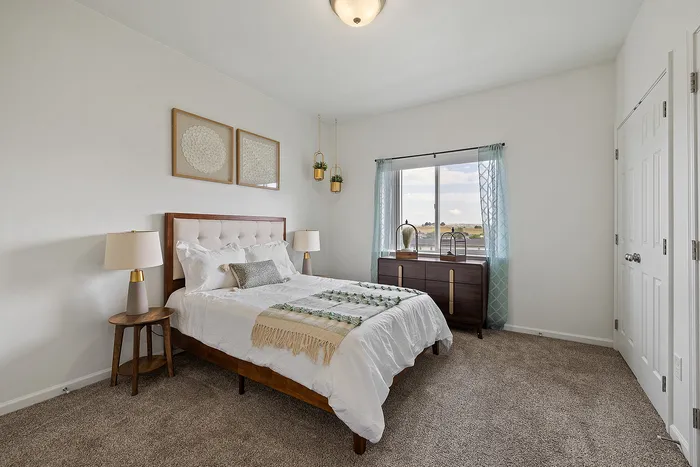 Bright and cozy bedroom featuring a plush bed, elegant bedside lamps, and large window with scenic views, accented by stylish decor and lush carpeting.