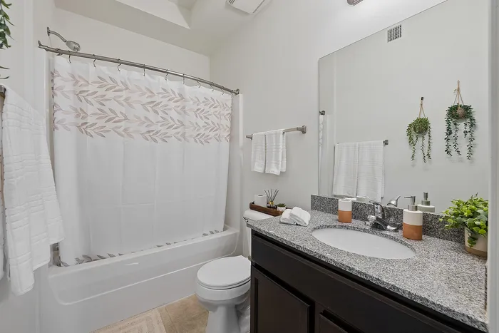 Contemporary bathroom with a stylish shower curtain, elegant dark wood vanity, and vibrant greenery accents.