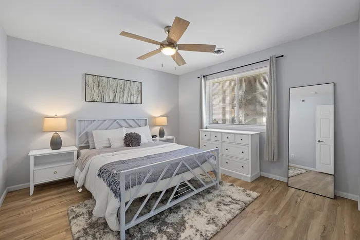 Bright and inviting bedroom with modern decor, featuring a cozy bed, stylish nightstands, ample natural light through large window, and elegant hardwood floors.