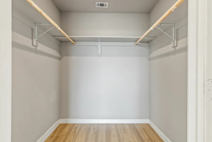 Spacious walk-in closet with elegant wooden flooring and ample hanging space.
