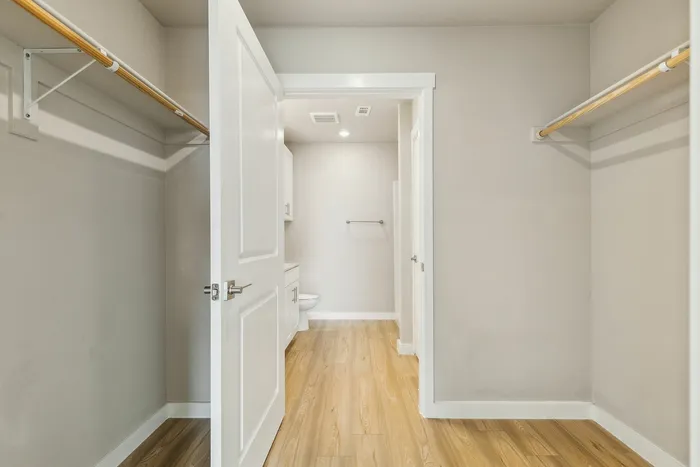 Spacious walk-in closet with elegant hardwood flooring and ample hanging space, leading to a bright, modern bathroom.