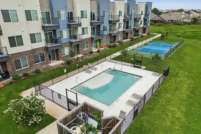 Modern apartment complex with a refreshing pool, charming balconies, and a vibrant tennis court, all set amidst lush green surroundings.