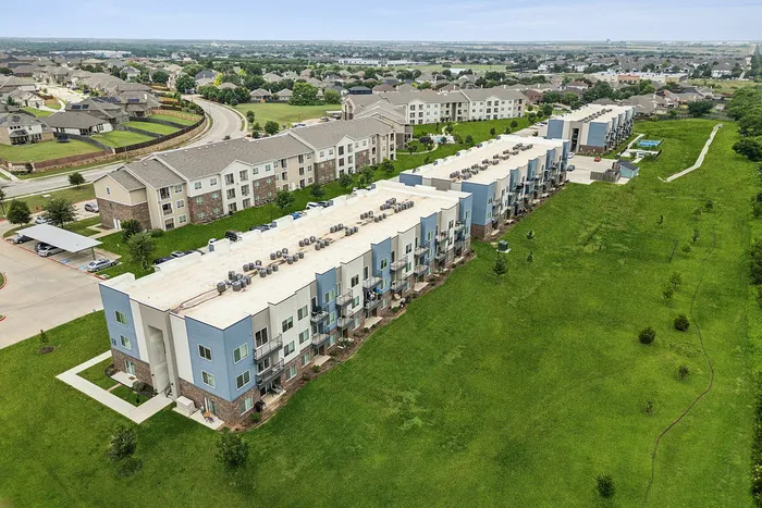 Aerial view of modern apartment complex surrounded by lush green lawns, showcasing spacious living areas with scenic neighborhood surroundings.