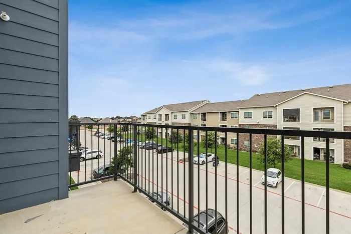 Inviting balcony view overlooking a well-maintained apartment complex with ample parking and lush greenery under a clear blue sky.
