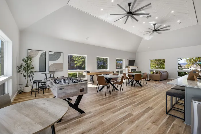 Bright and spacious community lounge with modern decor, featuring foosball and games tables, comfortable seating, and large windows with garden views.