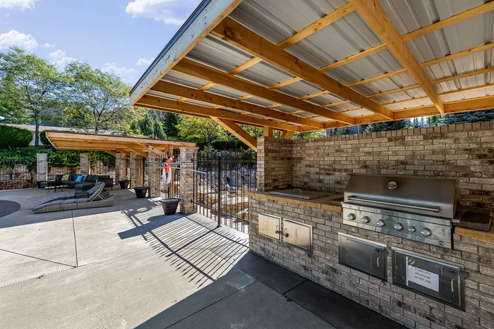 Inviting outdoor patio with modern grill and shaded seating area, surrounded by lush greenery and bright skies.