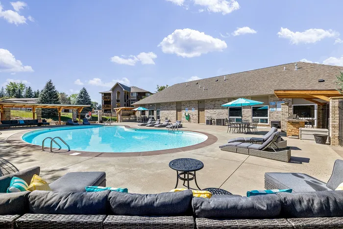 Inviting apartment complex pool area with sun loungers, vibrant umbrellas, and a cozy seating area, perfect for relaxation under clear blue skies.