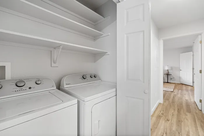 Chic laundry space featuring modern washer and dryer with practical shelving, tucked into a bright and airy corridor with elegant wood flooring.