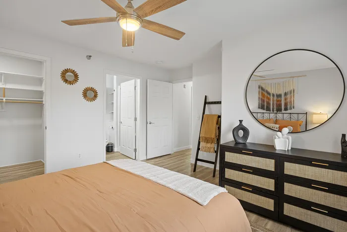 Elegant bedroom featuring a warm-toned bedspread, modern ceiling fan, and chic decor with a large mirror, creating a cozy and stylish ambiance.
