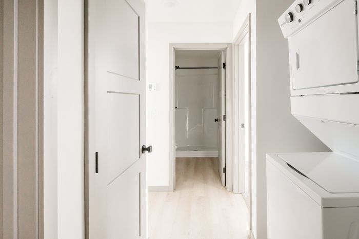 Bright hallway with modern laundry appliances and elegant light wood flooring leading to a sleek, contemporary bathroom.