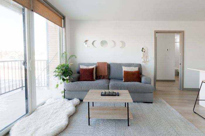 Bright and cozy living room featuring a sleek gray sofa with decorative cushions, a stylish coffee table, and large glass doors opening to a sunny balcony. Lush greenery adds warmth to the space.