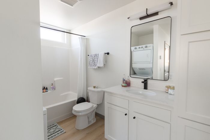 Bright, modern bathroom with sleek white cabinetry, integrated washer-dryer, and elegant fixtures, offering functionality and style.
