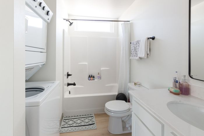 Bright, modern bathroom with sleek white fixtures, integrated washer-dryer, and a sophisticated shower-tub combination, perfect for comfort and convenience.