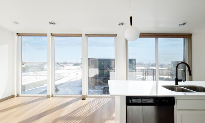 Bright apartment with large windows revealing a scenic snowy view, featuring a modern kitchen island with a sleek black faucet and stainless steel appliances.