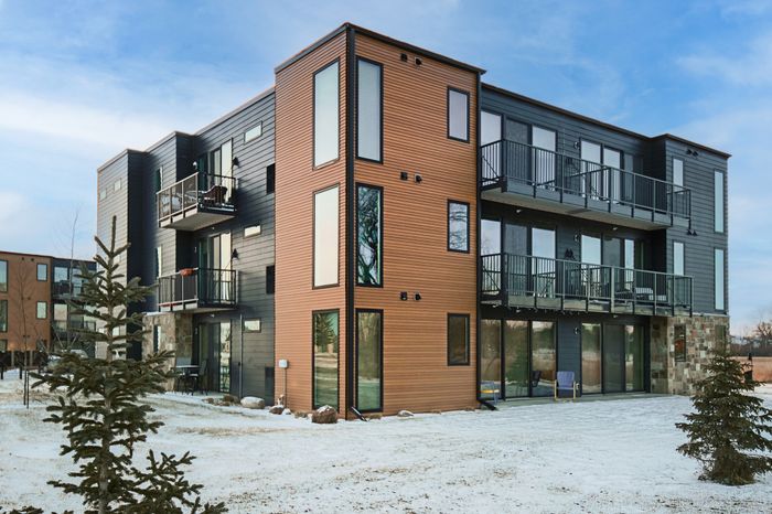 Modern apartment building with sleek exterior design and multiple balconies, set against a clear blue sky and snowy landscape.