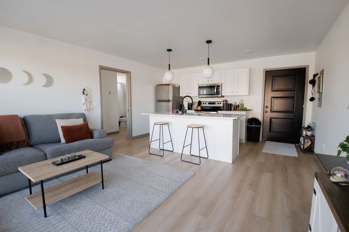 Chic modern apartment living area featuring a cozy sofa, stylish kitchen island with bar stools, and sleek contemporary decor.