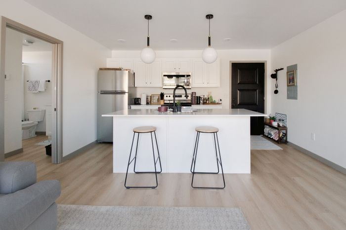 Modern kitchen with sleek white cabinetry, stainless steel appliances, and an inviting island with bar stools, complemented by stylish pendant lighting and light wood flooring.